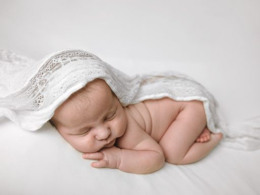 RECIEN NACIDO EN BARCELONA Y ALREDEDORES Bebé dormido sobre una superficie blanca con una manta ligera cubriéndolo parcialmente.