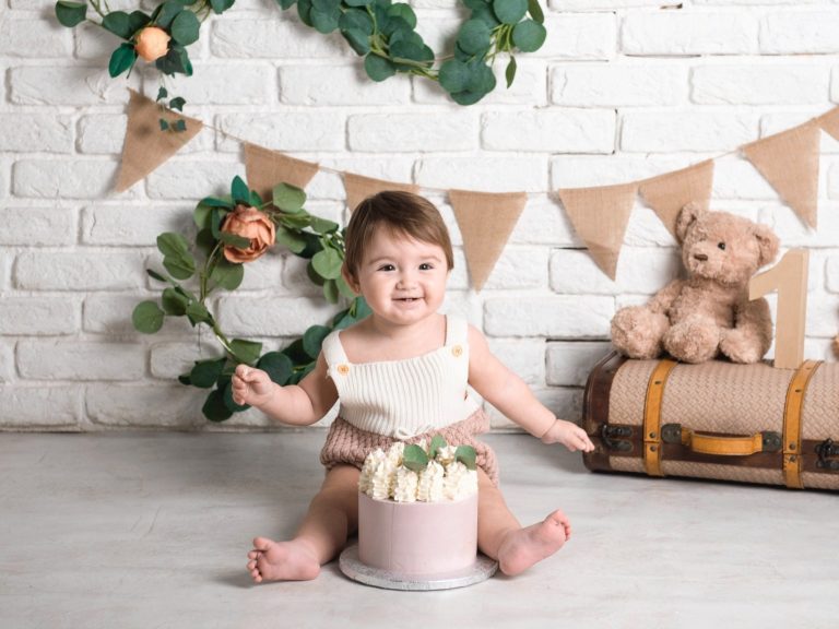 img source='pic.gif' alt=SESIONES SMASH CAKE BARCELONA Niño pequeño sentado frente a un pastel decorado, rodeado de plantas y adornos.